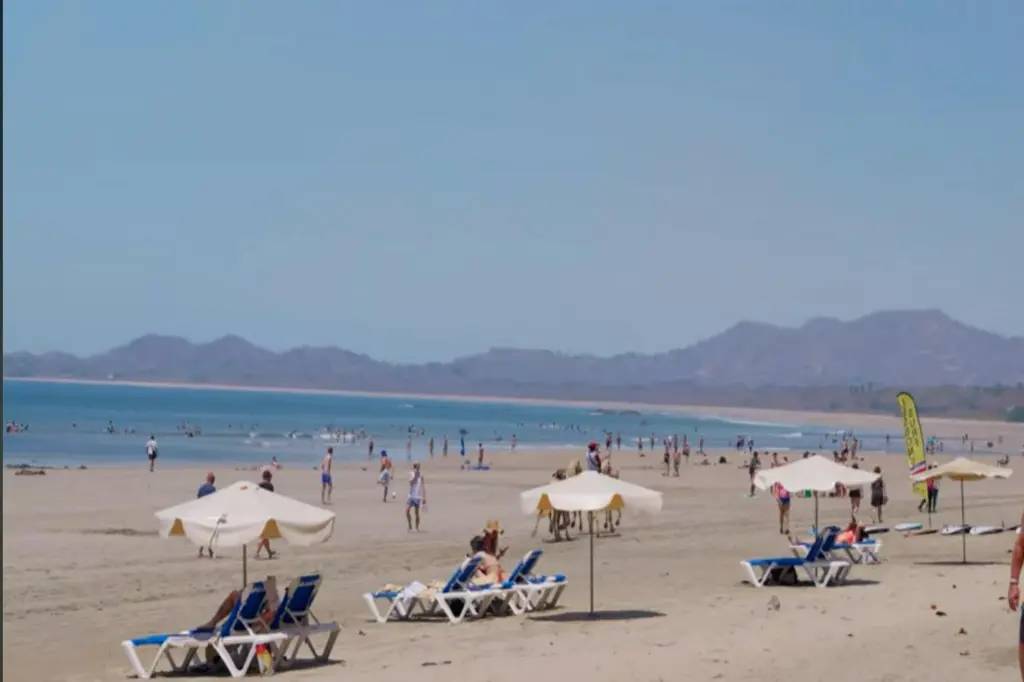 Beachgoers and sun loungers on Playa Tamarindo, Costa Rica, with the Guanacaste hills beyond